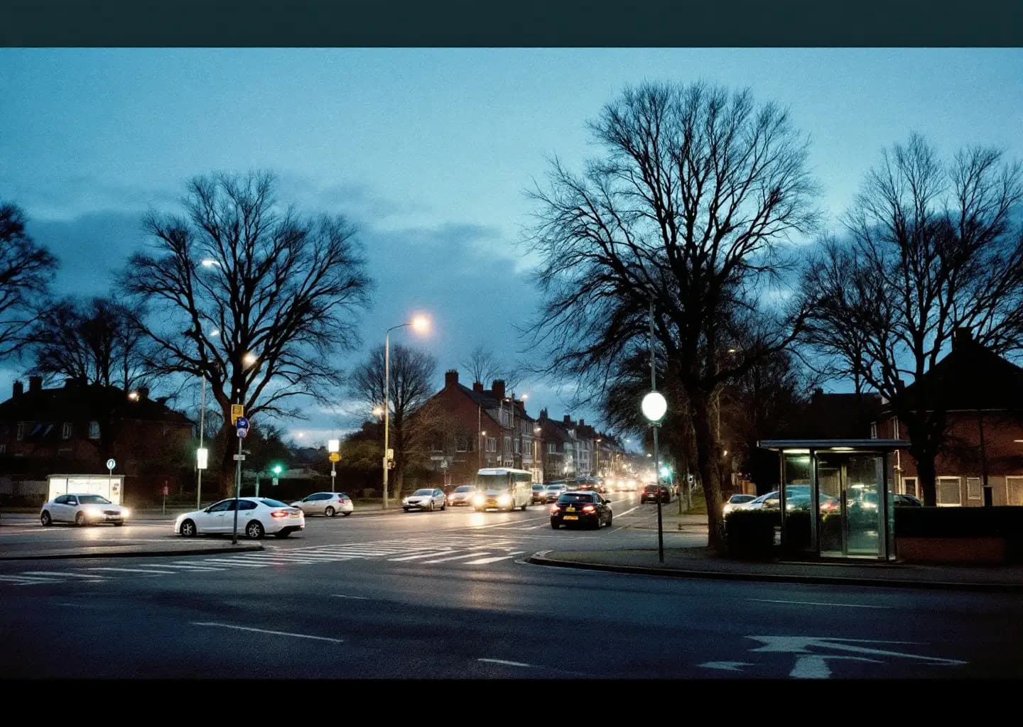 Carrefour de banlieue en fin de journée, phares des voitures à l'arrêt et abri de bus à l'heure bleue