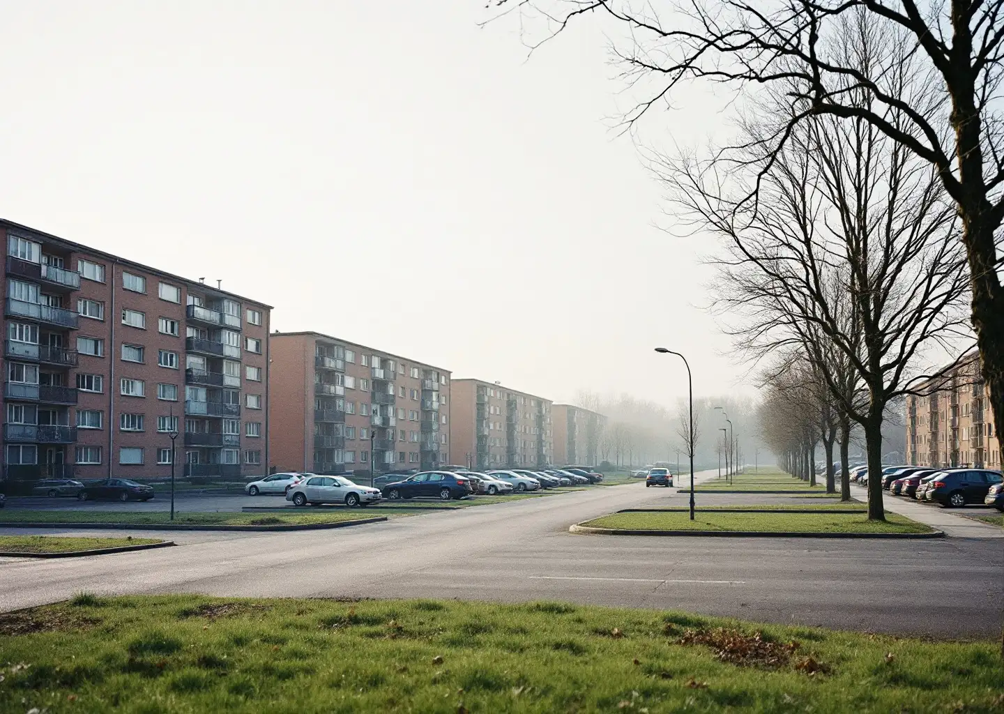 Barres d'immeubles à balcons des années 1970 et vaste parking de résidents au petit matin